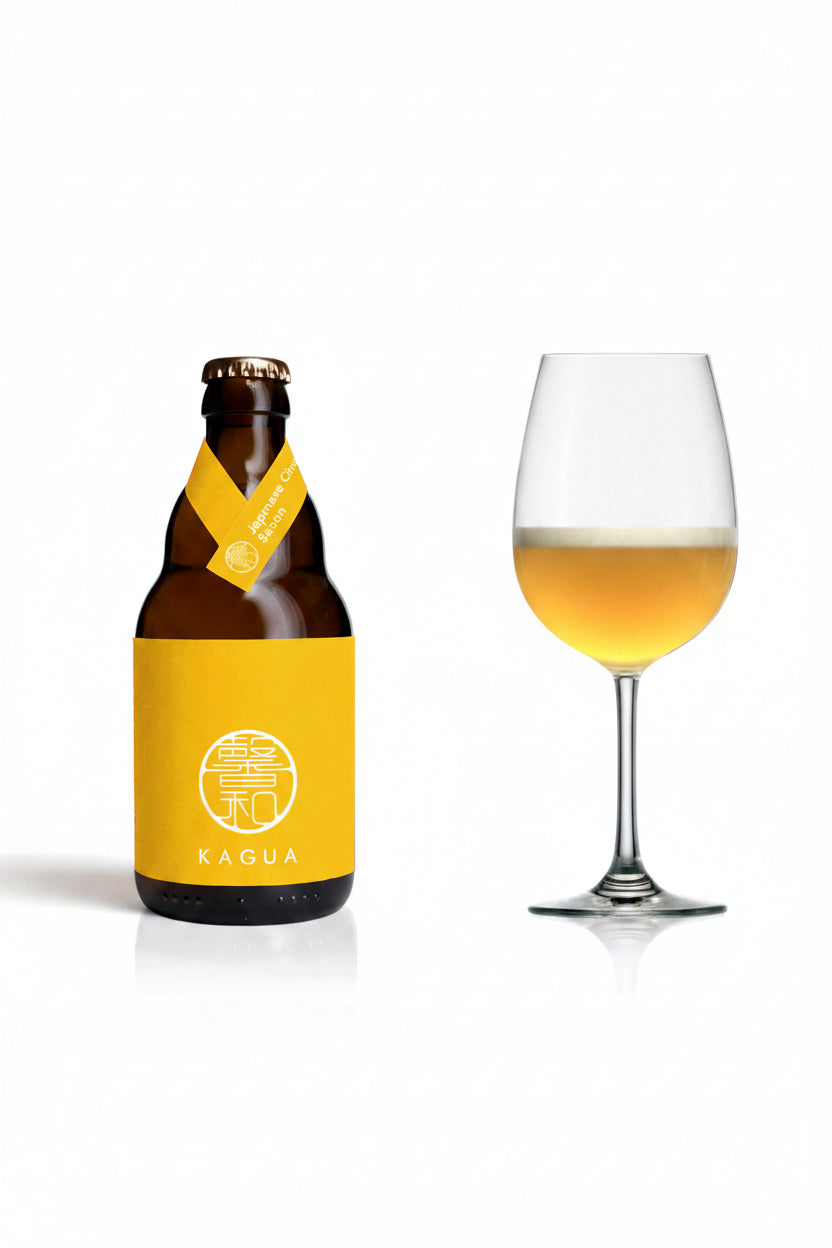 A bottle of Kagua beer with a bright yellow label and neck ribbon stands next to a stemmed wine glass filled with the golden beer, on a clean white background.